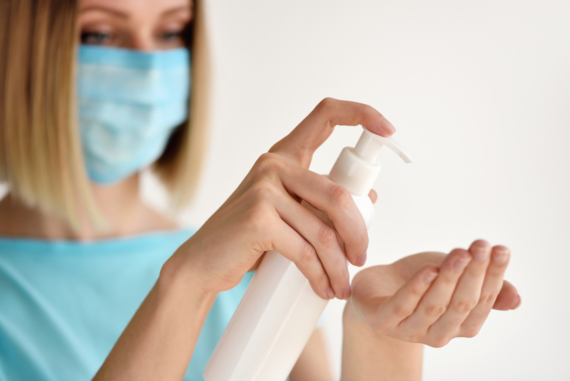 Young woman using antiseptic gel and wearing prevention mask